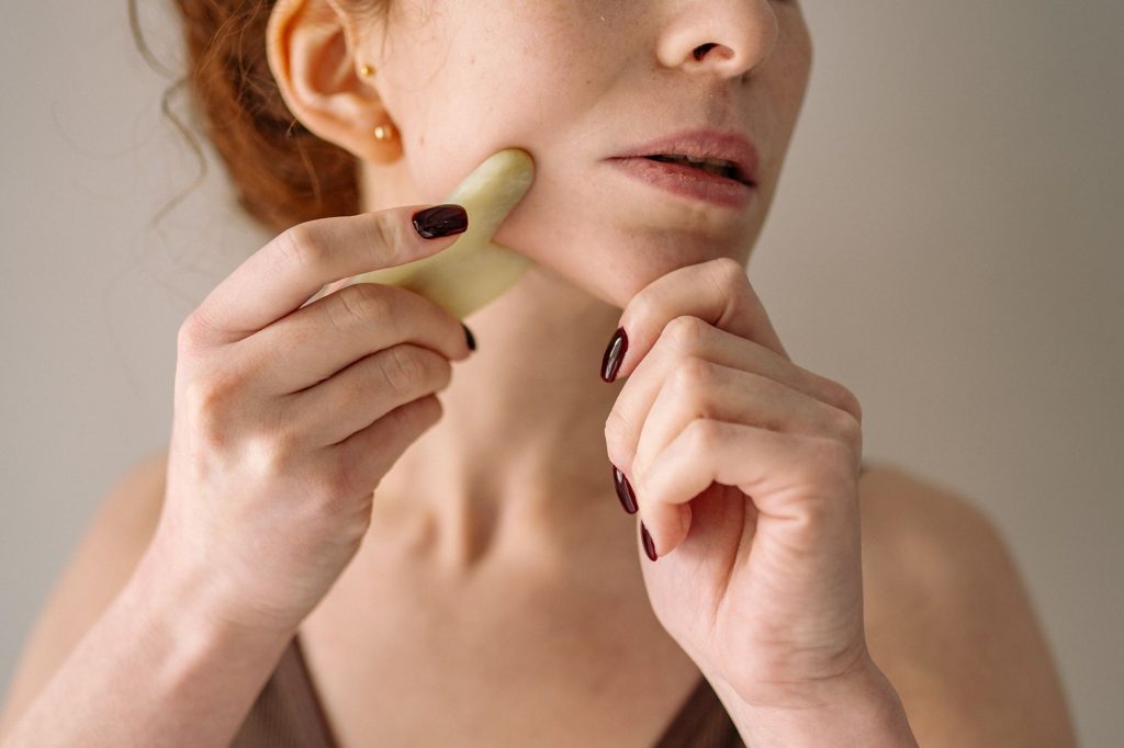 Gua Sha – Woman using tool on face in natural light.