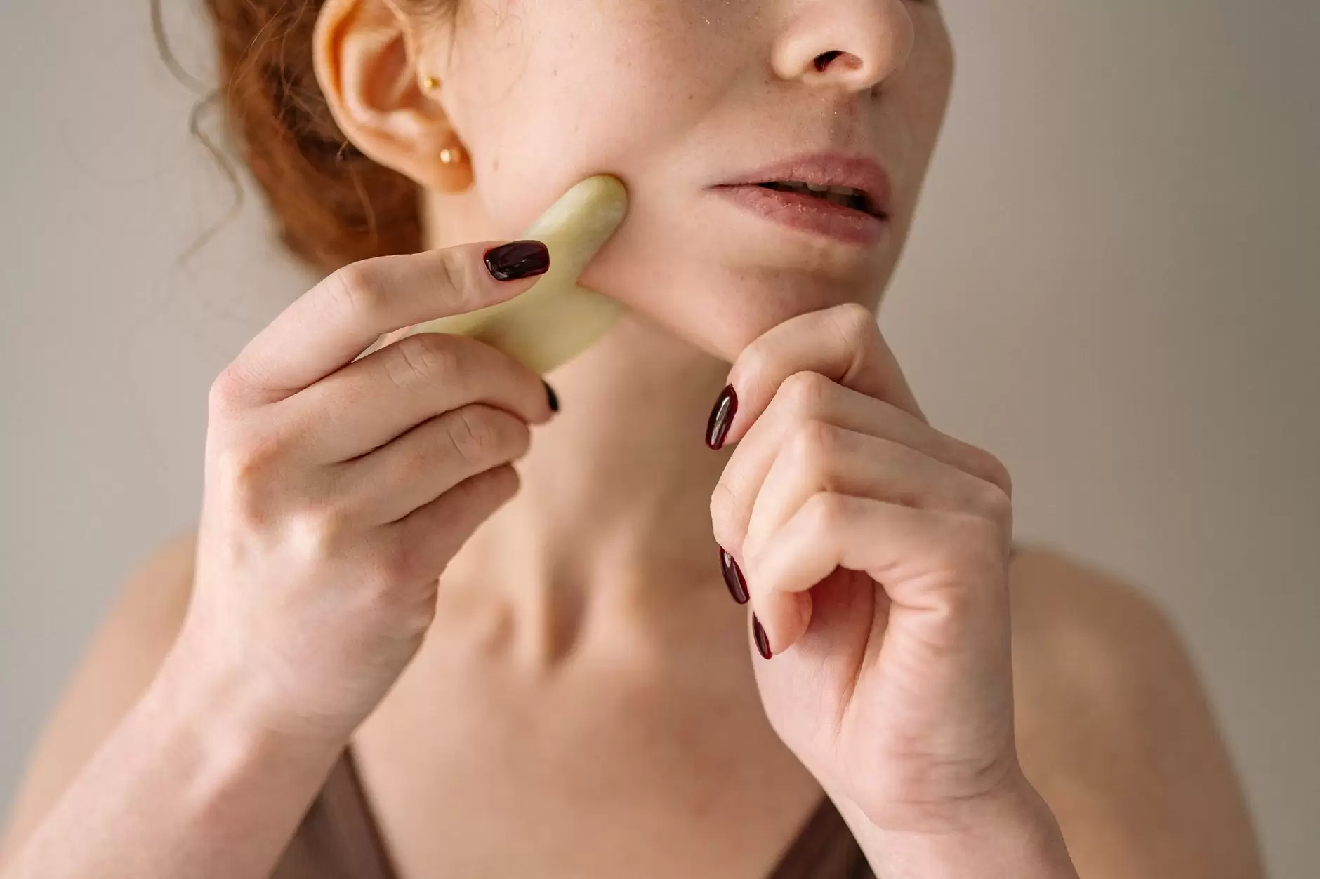 Gua Sha – Woman using tool on face in natural light.